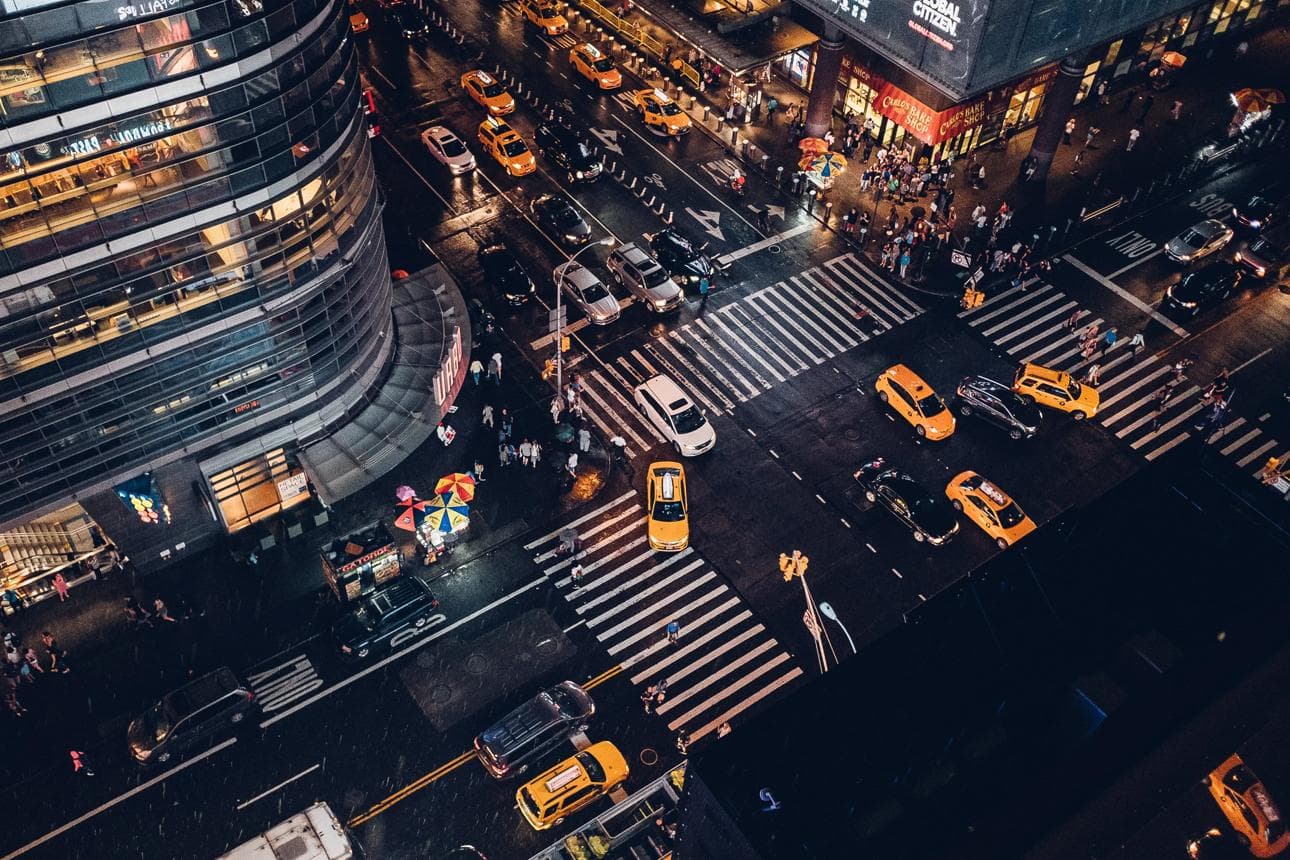 An urban intersection at night with vehicles and pedestrians moving through several approaches.